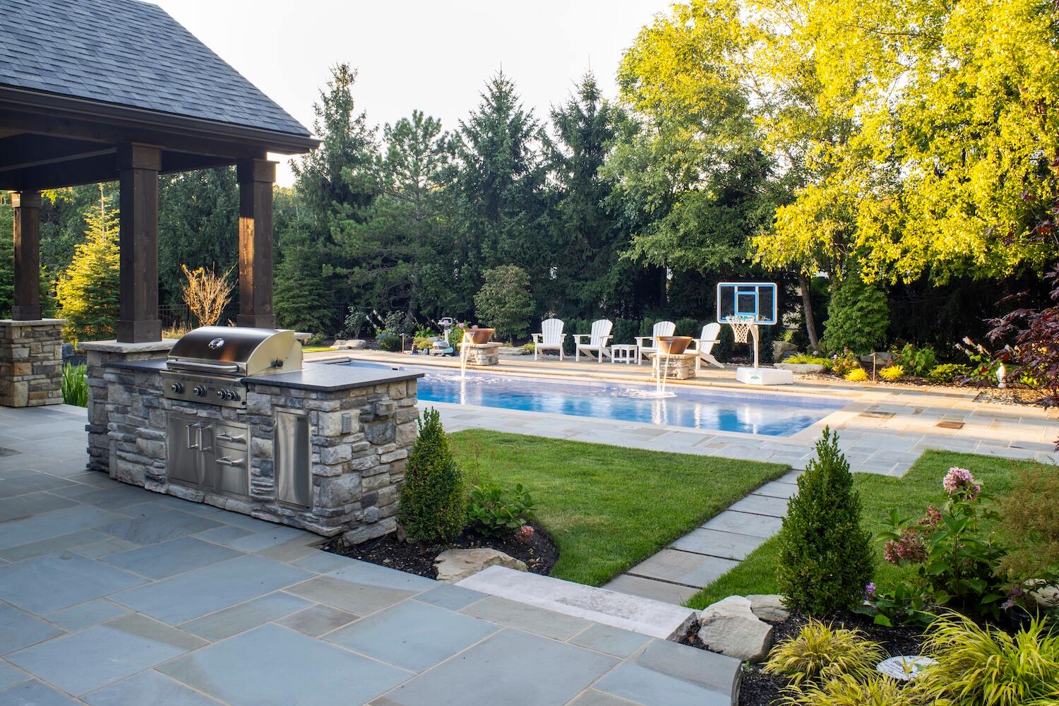Backyard outdoor kitchen with stone grill island, pool, and seating area in Ohio landscape design