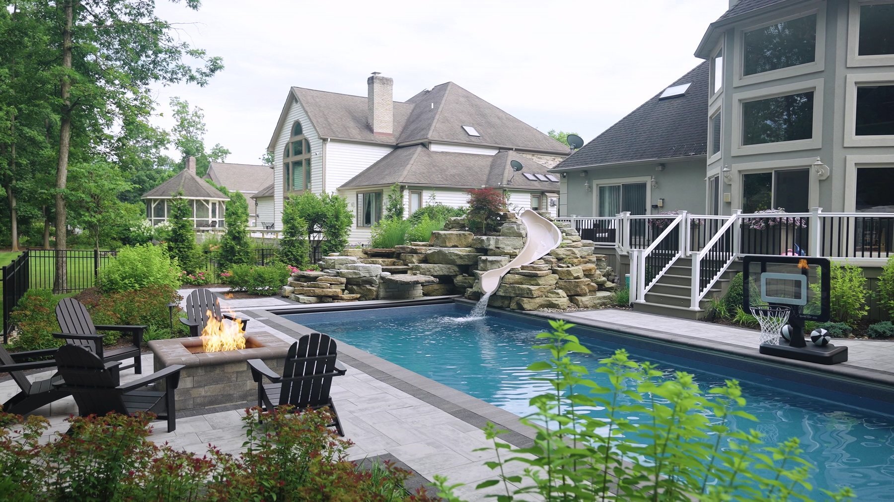 Backyard pool with fire table, stone waterfall and slide by Exscape Group