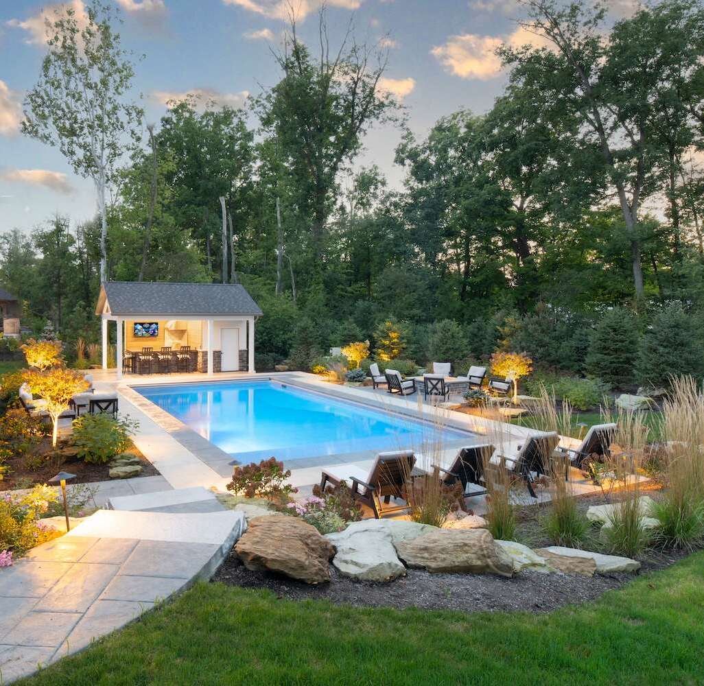 Backyard pool with pool house, patio seating, and landscape lighting in Aurora OH
