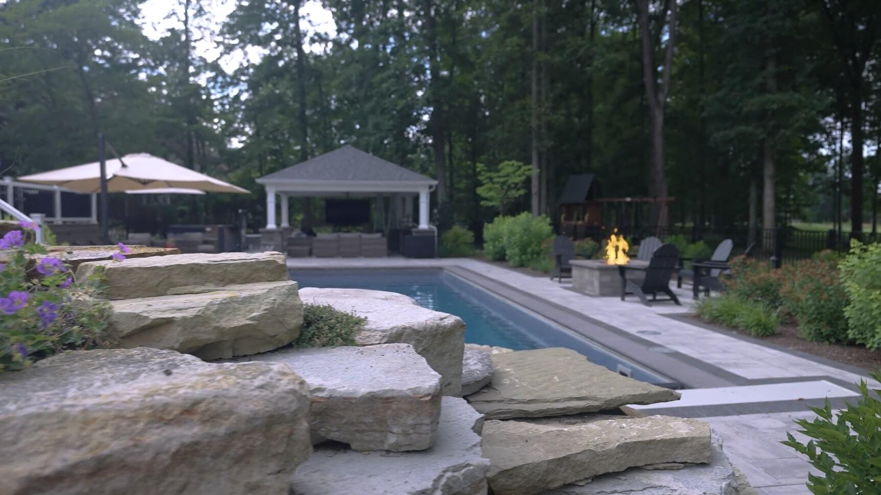 Backyard pool with stone steps, fire pit, and covered pavilion in Pepper Pike OH