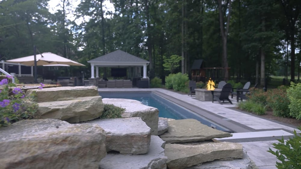 Backyard pool with stone steps, fire pit, and covered pavilion in Pepper Pike OH