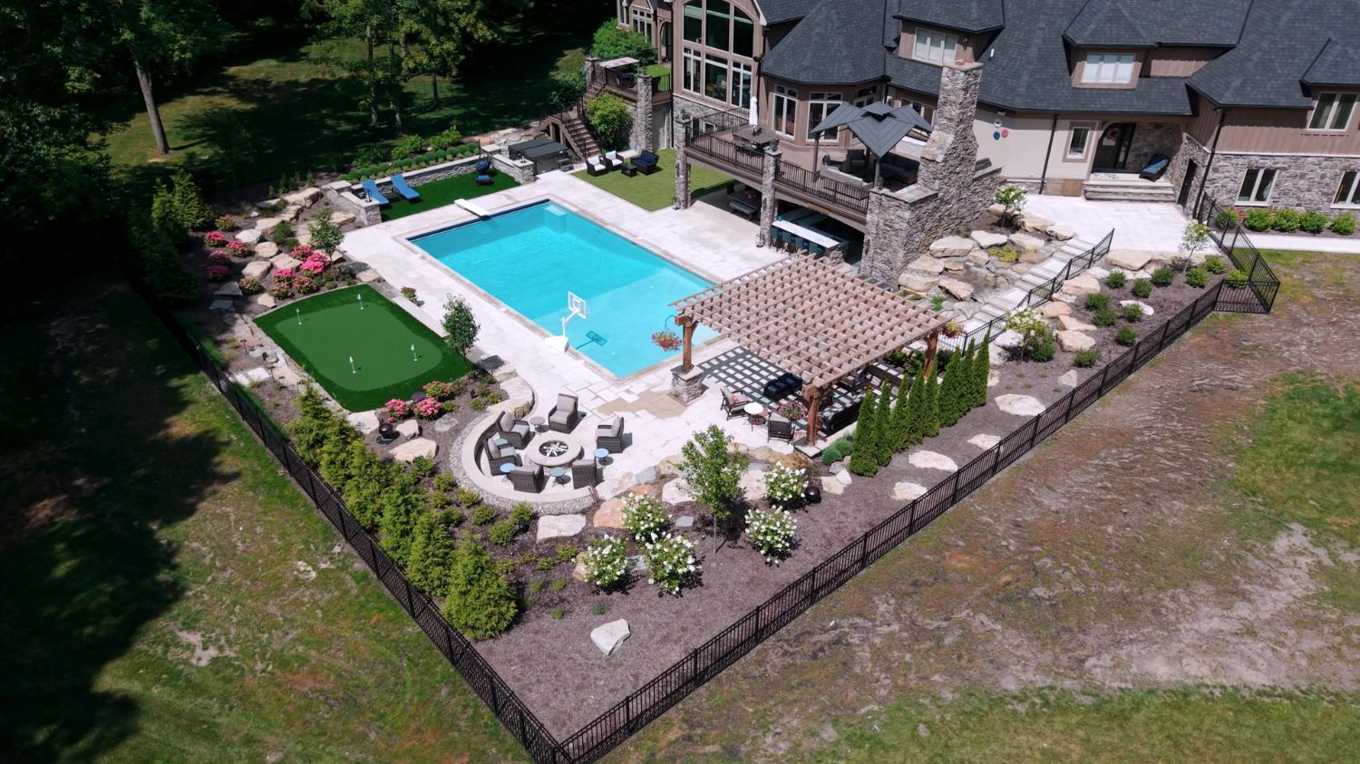 Aerial view of a backyard pool with paver patio, pergola, and artificial turf