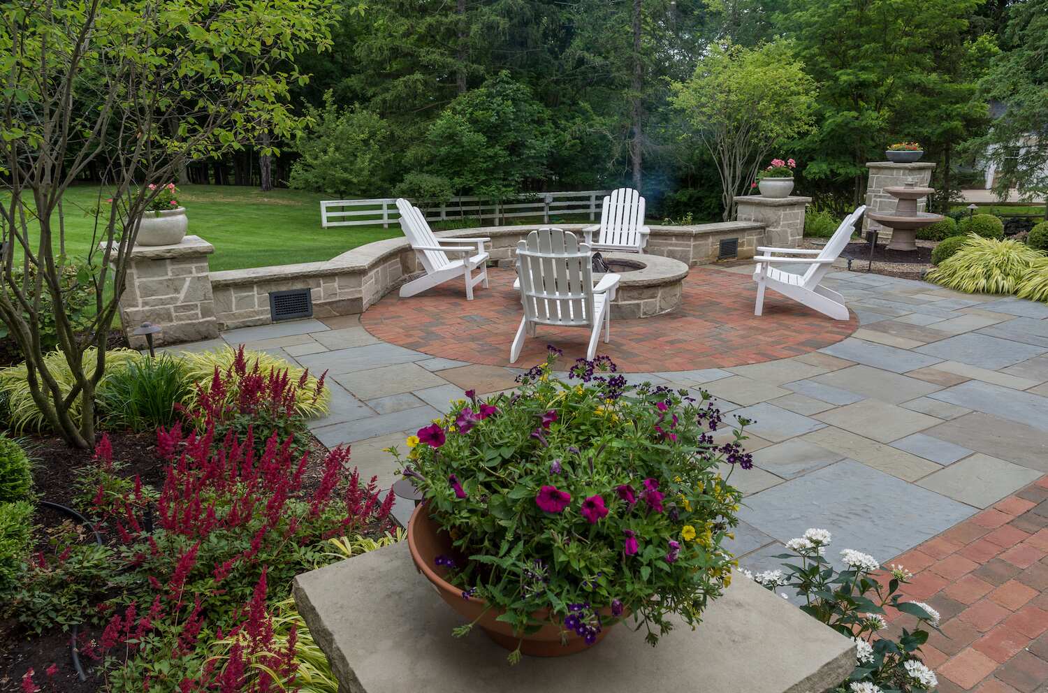 Stone patio with Adirondack chairs, flower planters, and a fire pit