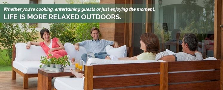 A group of adults sitting in pairs across from each other in a very clean and tidy outdoors patio with cushioned wooden benches smiling at each other with text reading 