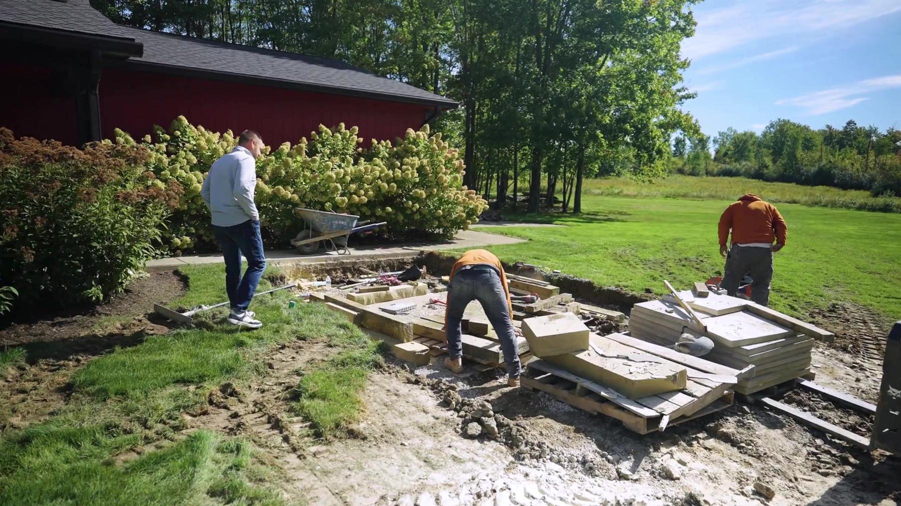 Exscape Group crew installing a stone patio beside a red barn
