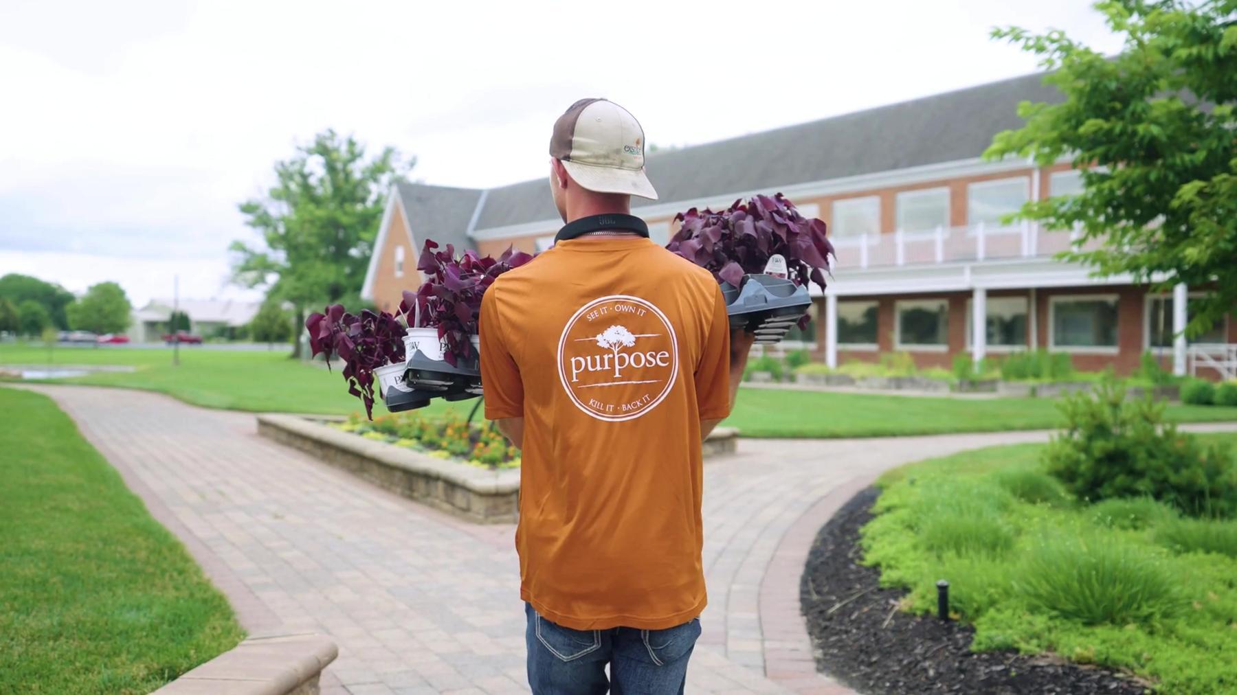 Exscape Group crew member carrying flats of plants across a commercial property