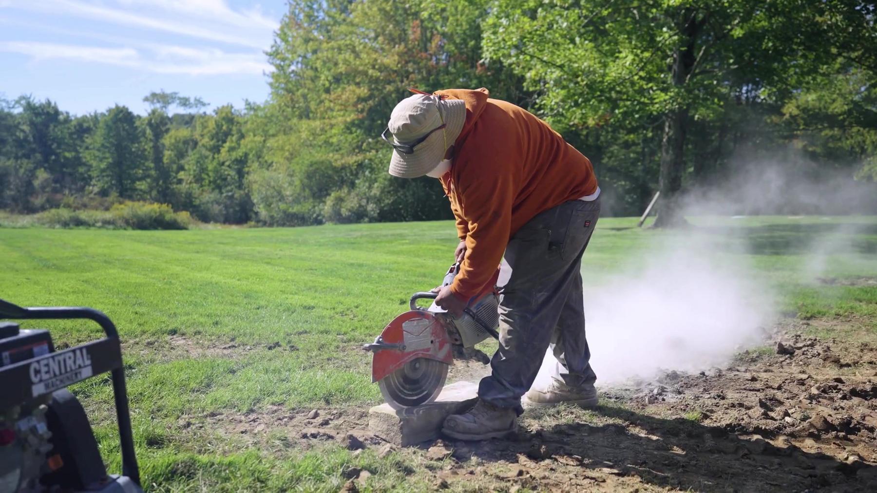 Exscape Group crew member cutting stone with a concrete saw on a lawn
