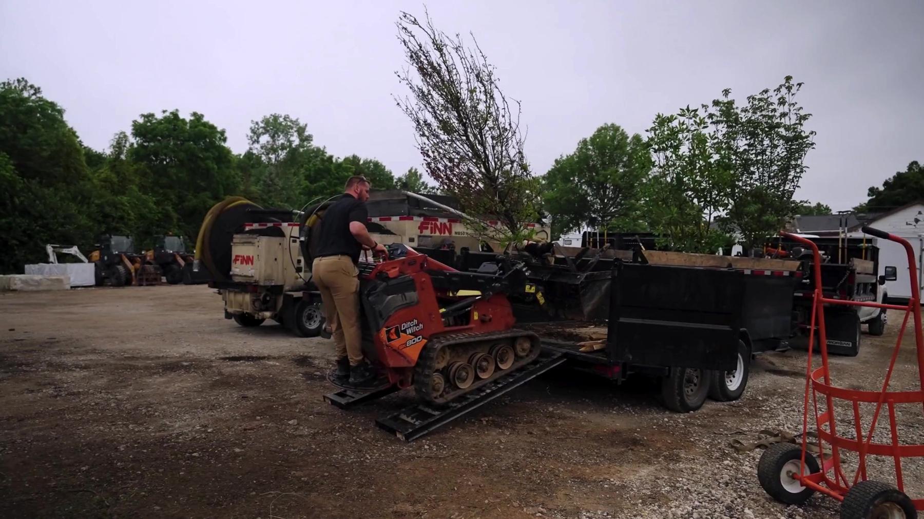 Exscape Group crew member driving a compact track loader onto a trailer