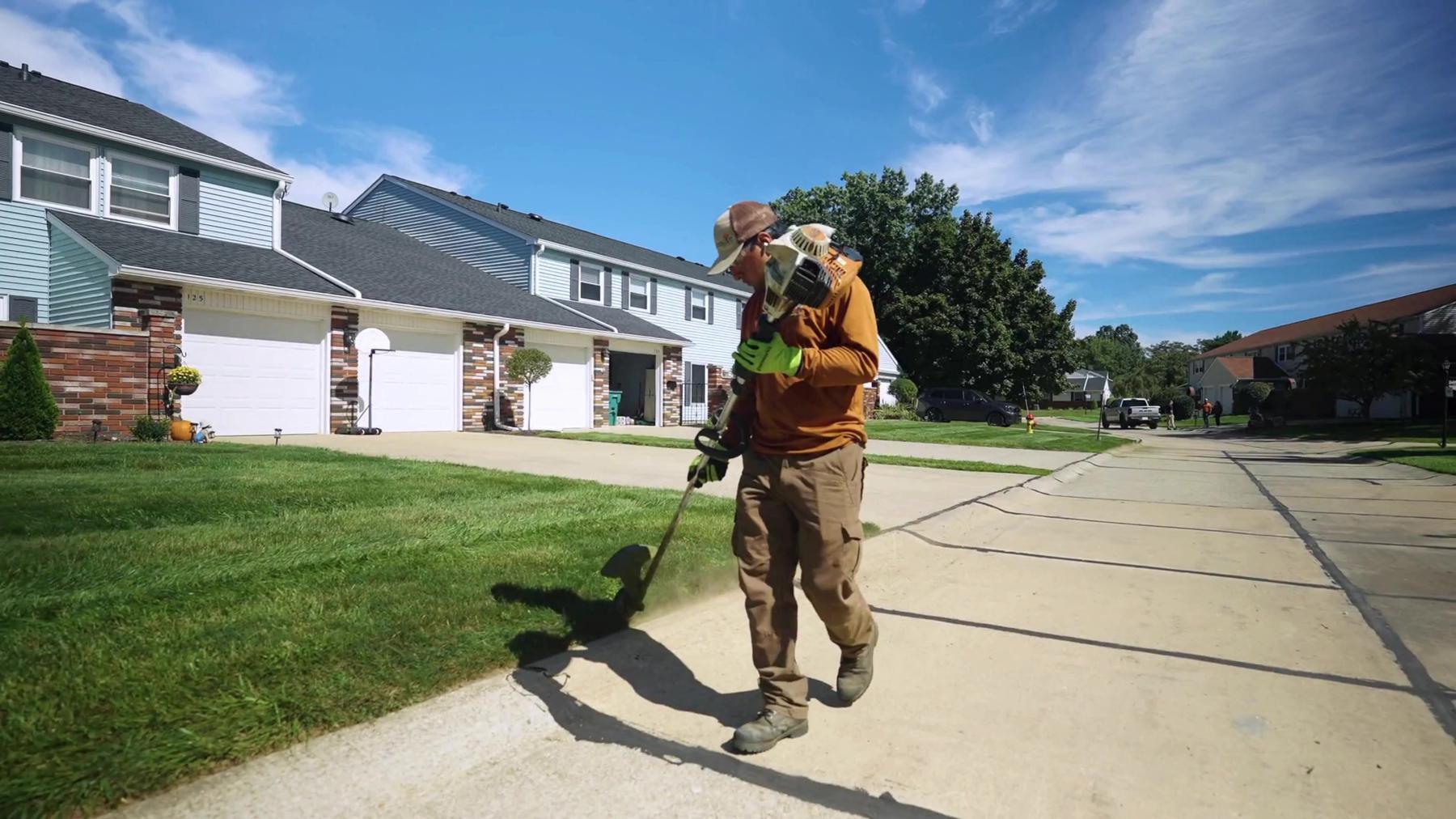 Exscape Group crew member edging a lawn along a sidewalk with a string trimmer