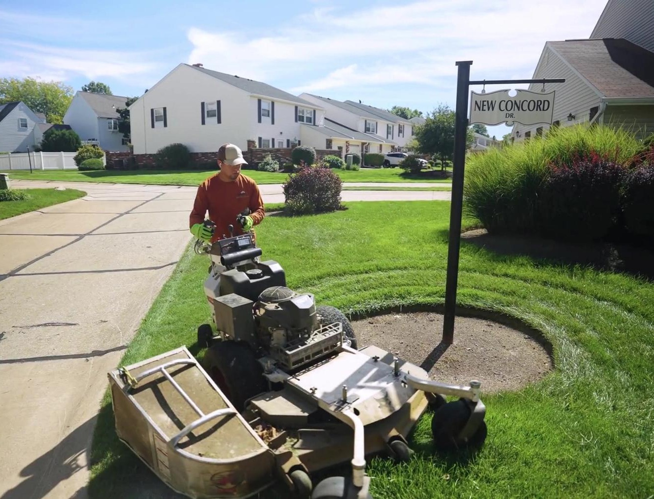 Exscape Group crew member mowing a community entrance with a walk behind mower