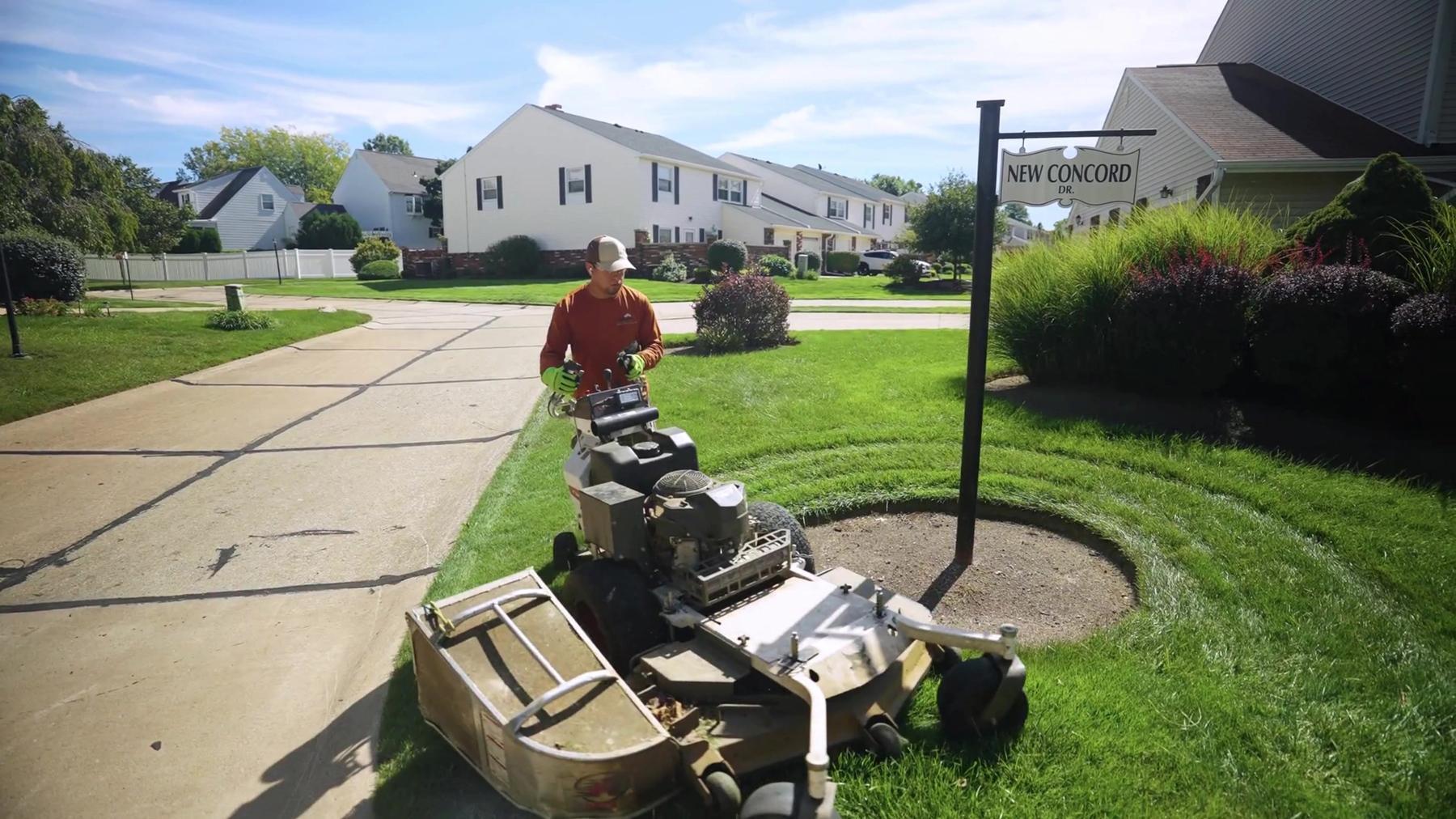 Exscape Group crew member mowing a community entrance with a walk behind mower