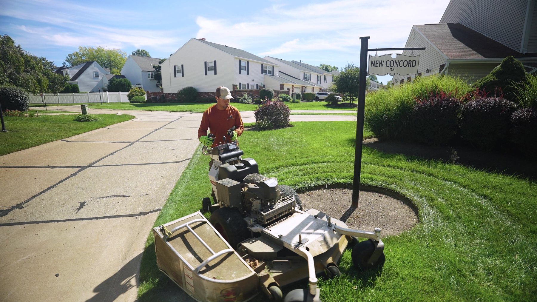 Exscape Group crew member mowing a community entrance with a walk-behind mower