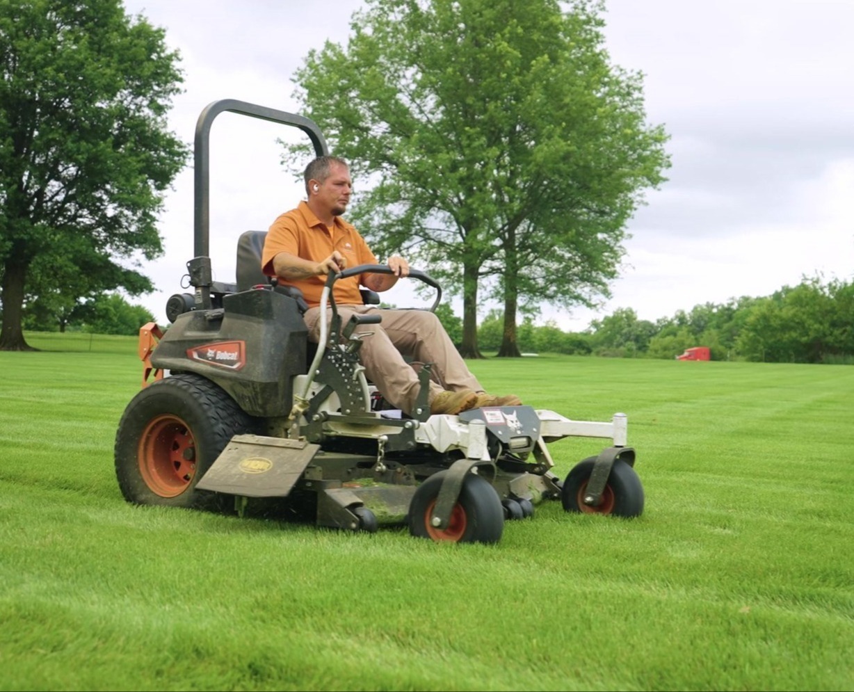 Exscape Group crew member mowing a large lawn on a zero-turn mower