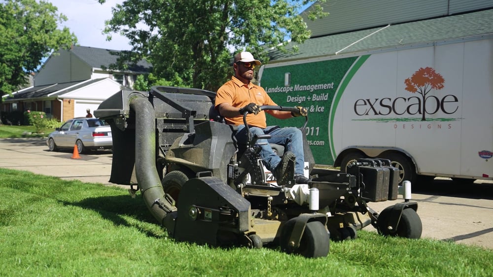 Exscape Group crew member on a stand-on mower beside a company trailer