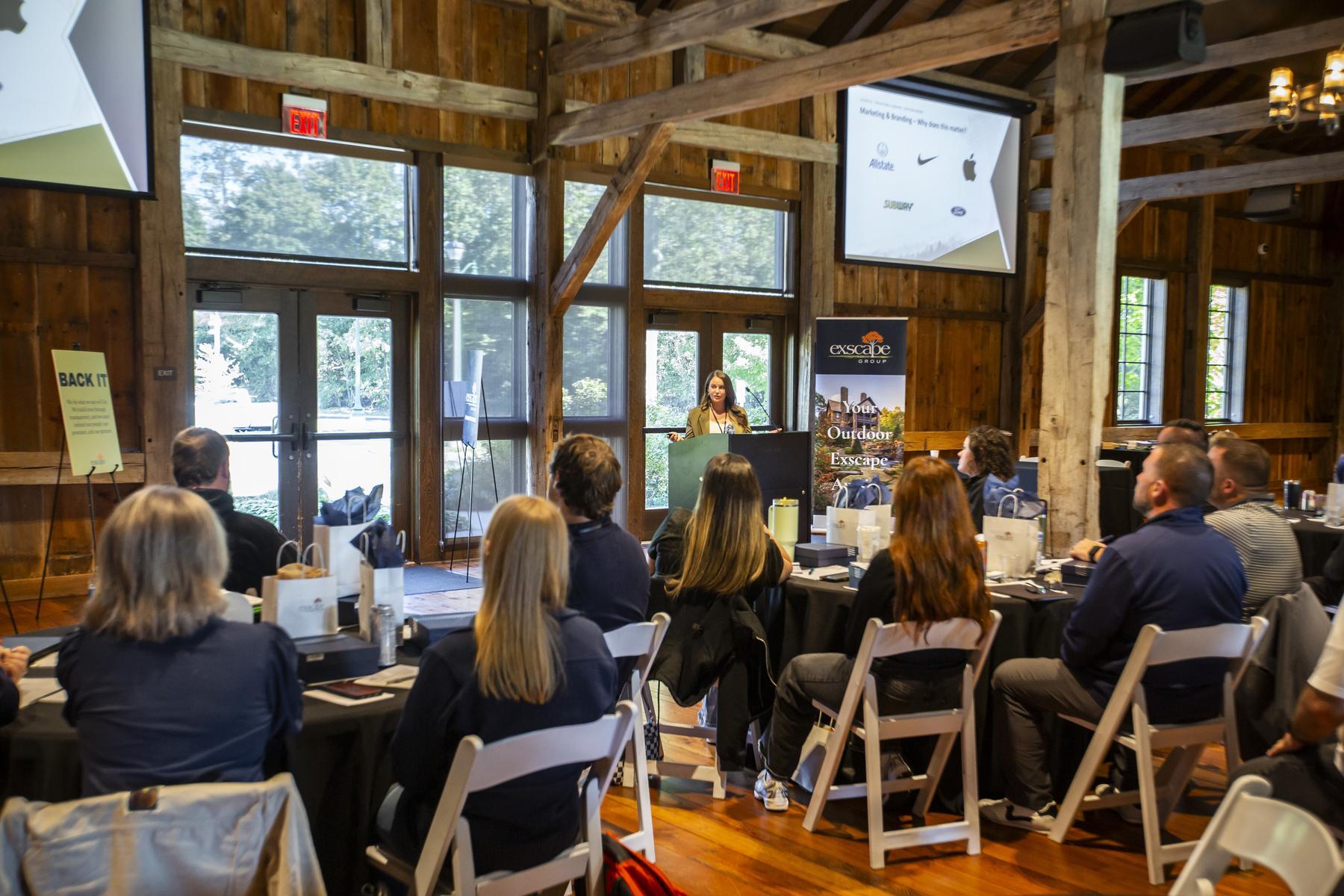 Exscape Group employees watching a presentation in a barn venue with tall windows