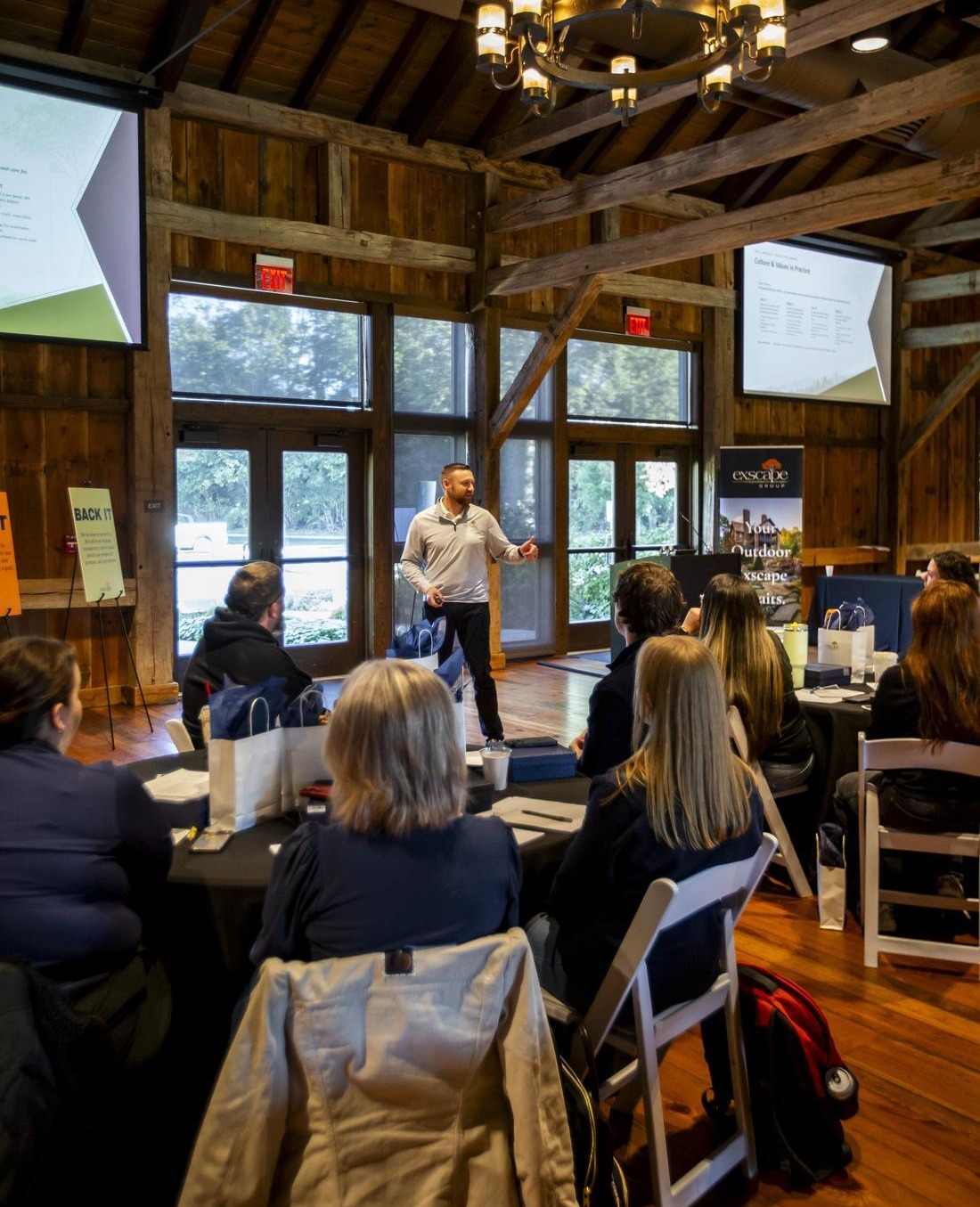 Exscape Group leader presenting under a wrought iron chandelier in a timber frame barn