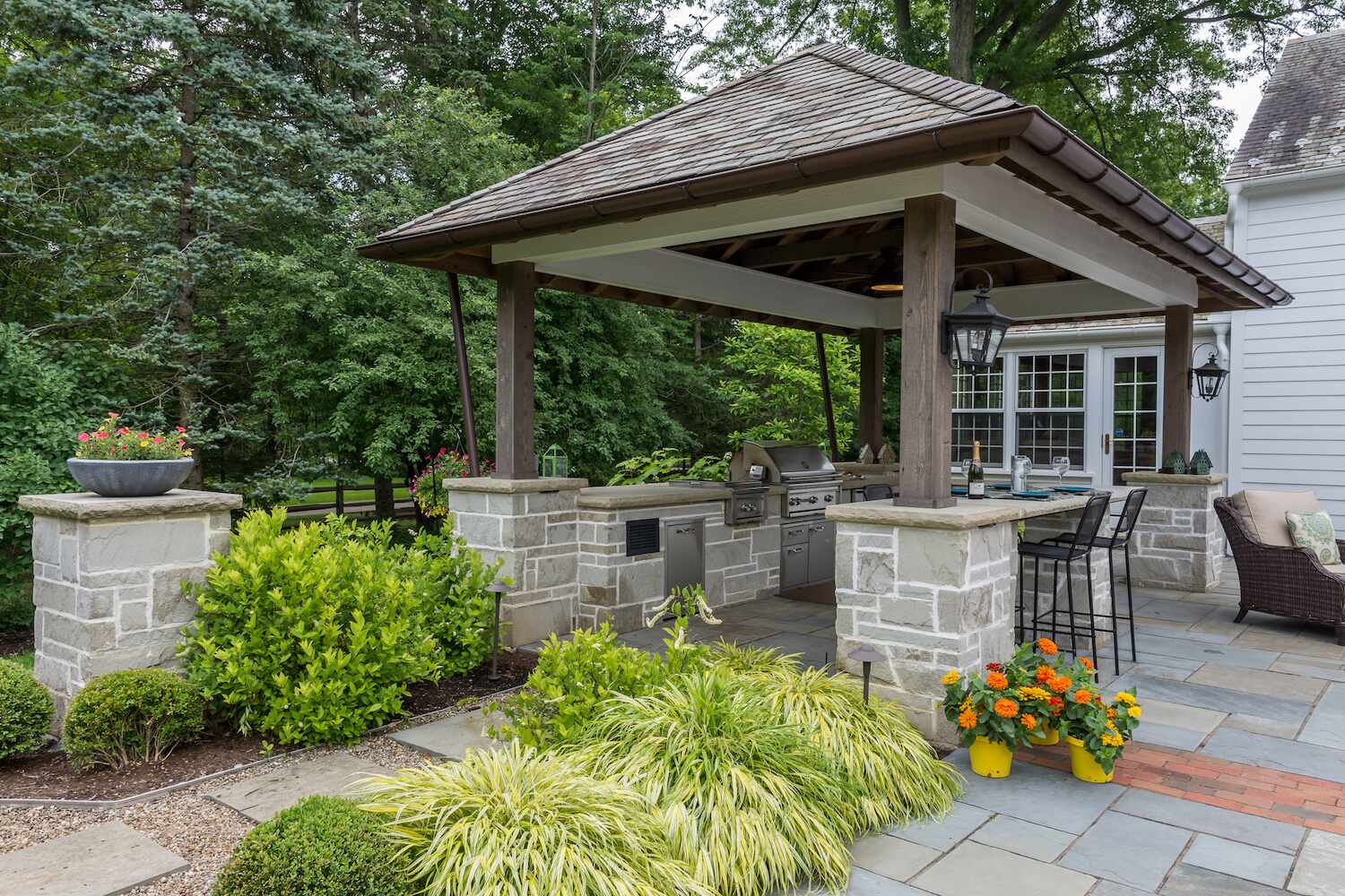 Covered backyard pavilion with stone columns and outdoor kitchen by Exscape Group in Moreland Hills, OH