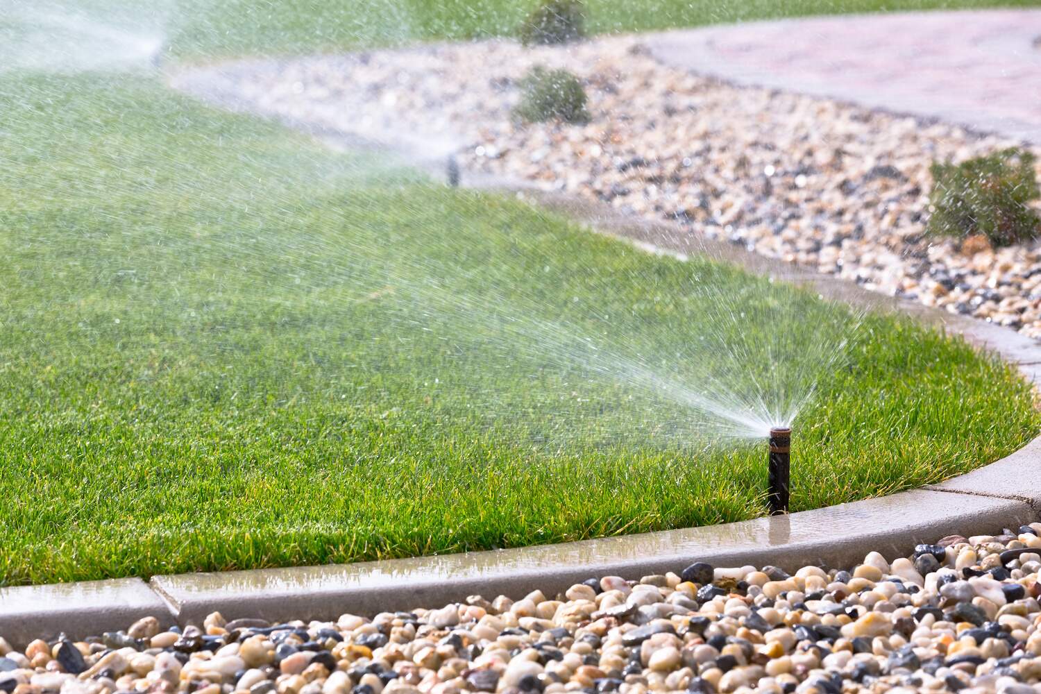 Irrigation sprinkler heads watering a residential lawn along a stone border by Exscape Group in Aurora, OH