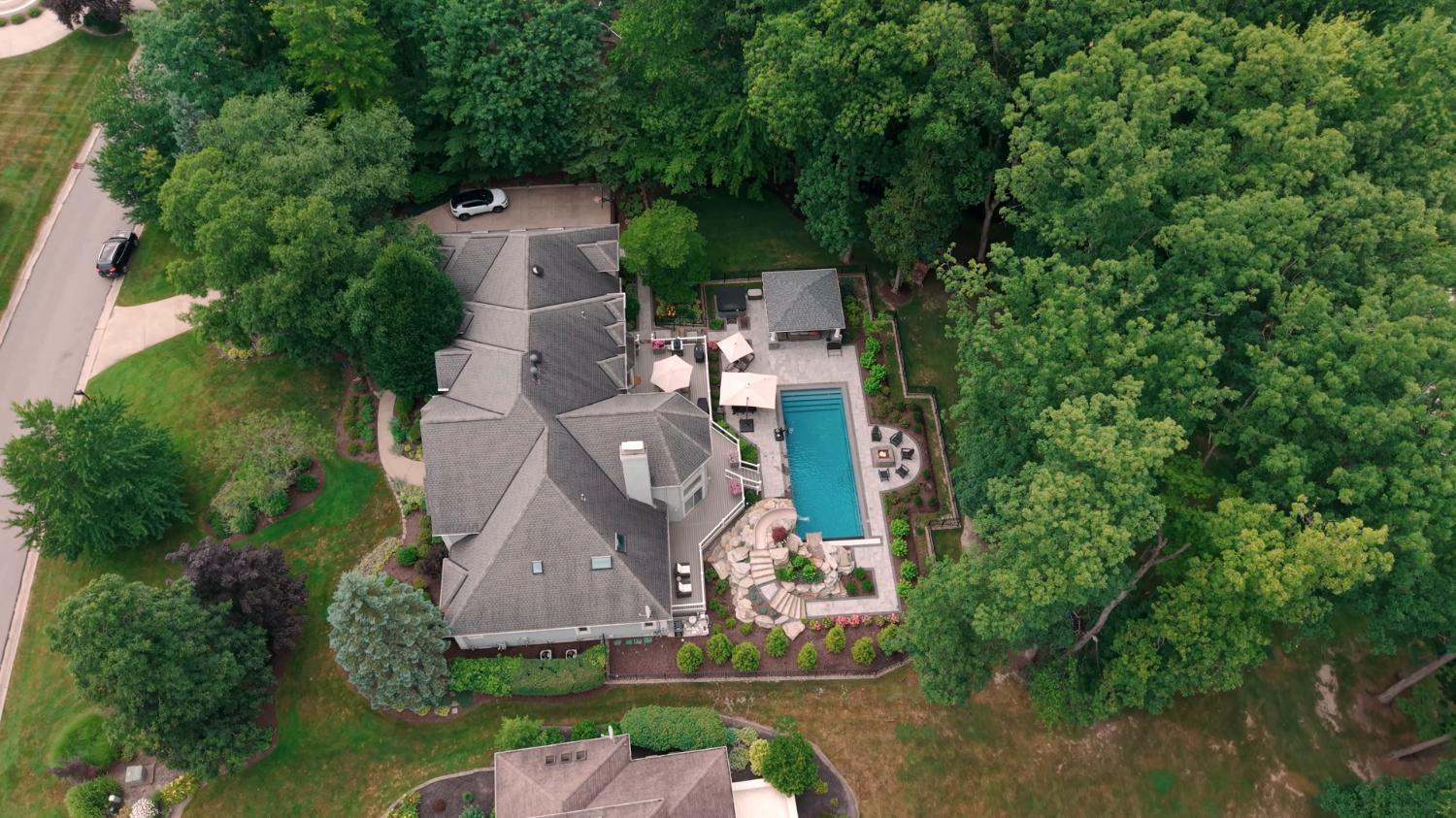 Aerial view of a backyard pool and deck surrounded by mature trees