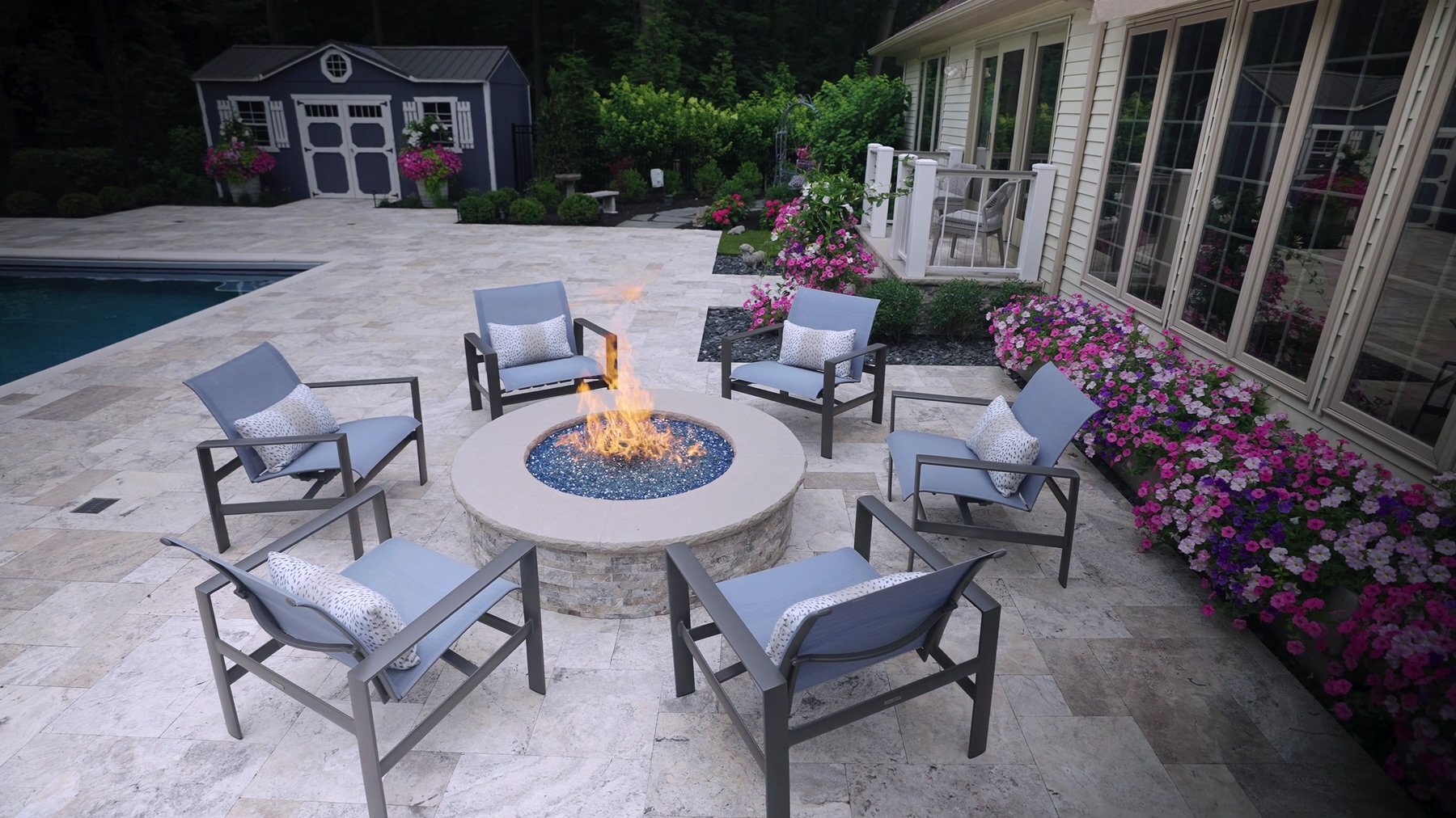Fire pit seating area beside a pool and flower beds by Exscape Group