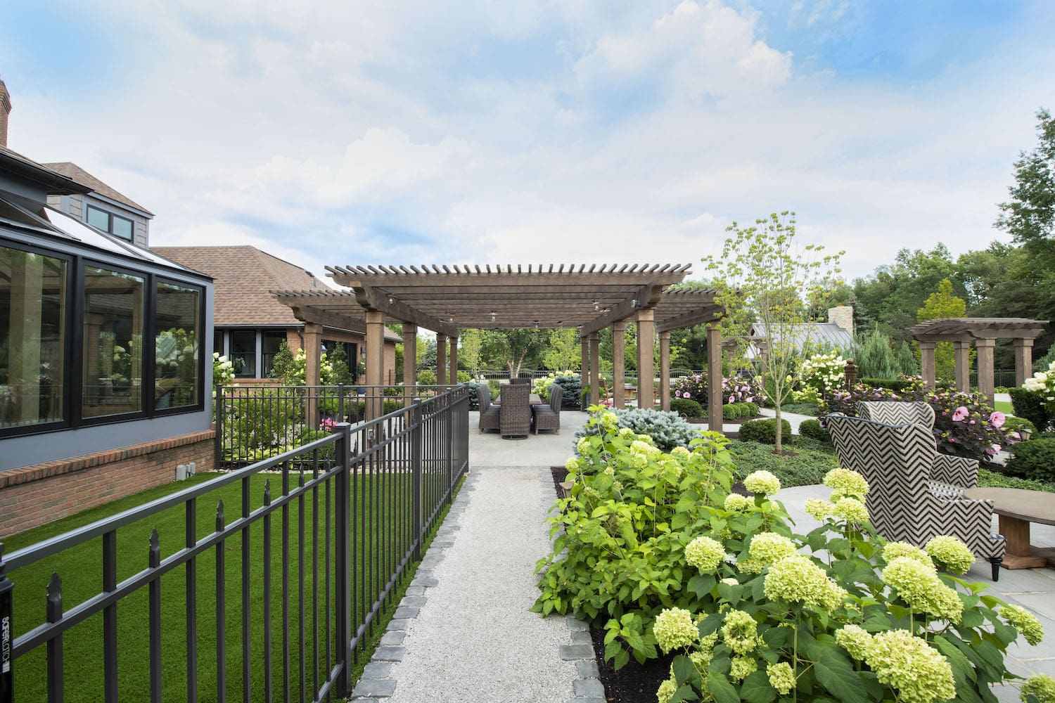 Garden walkway leading to a covered pergola dining area surrounded by hydrangeas and lush landscaping in Ohio.