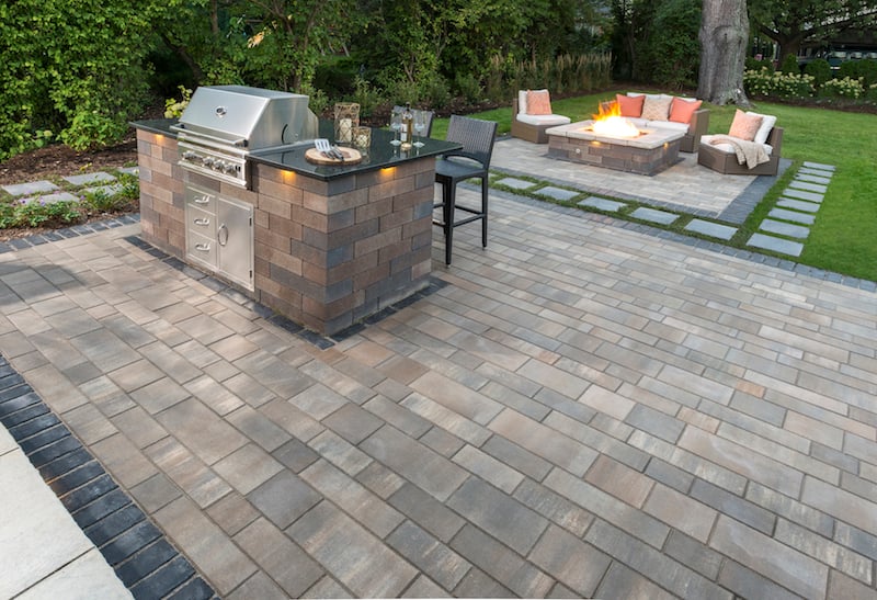 Built-in grill island on a paver patio with fire pit seating beyond