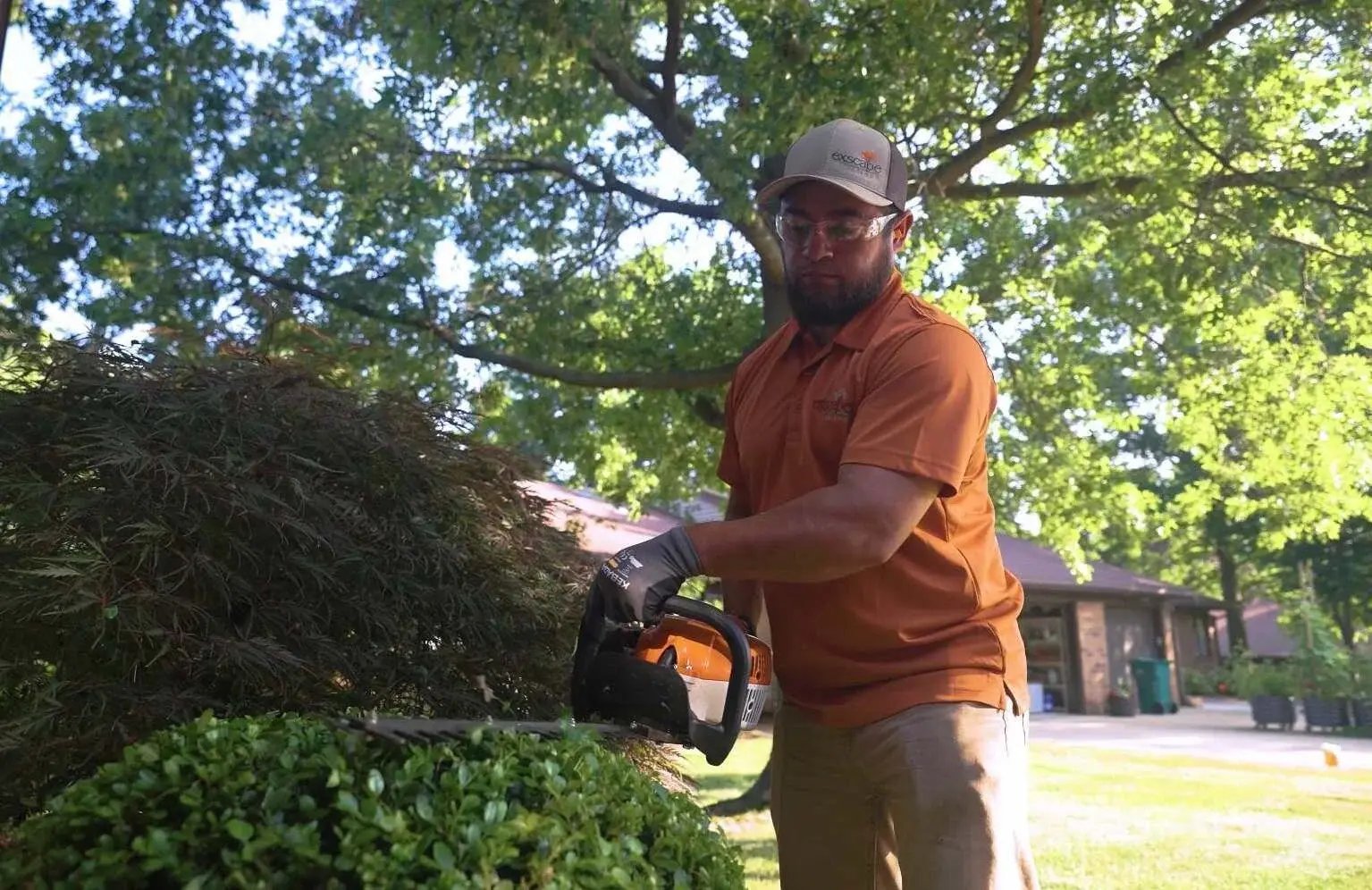 Landscape professional trimming bushes with hedge trimmer at a residential property in Ohio – Exscape Group landscaping services