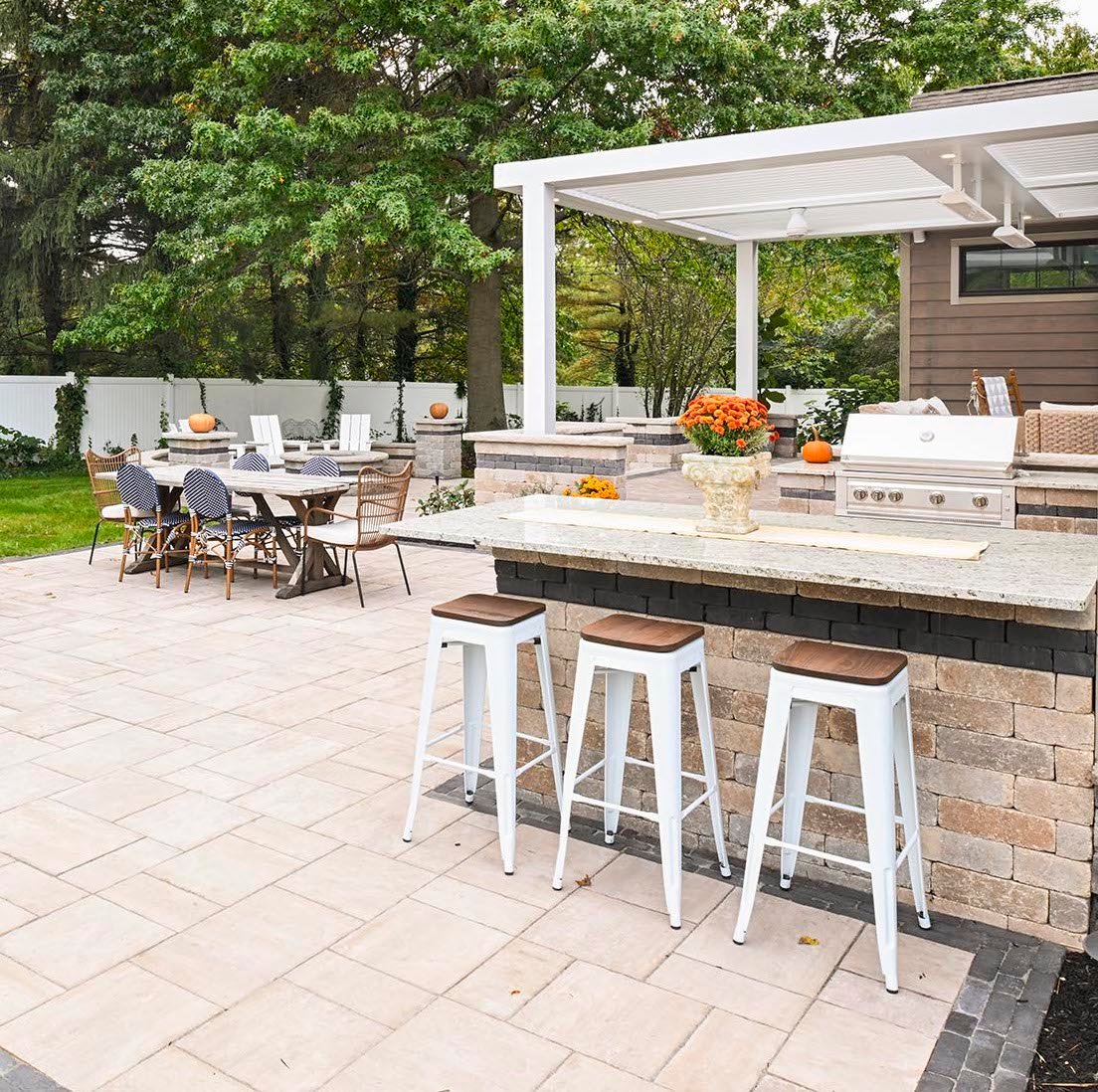 Outdoor kitchen and dining patio with built-in grill, bar seating, and modern pergola in a landscaped backyard in Ohio.