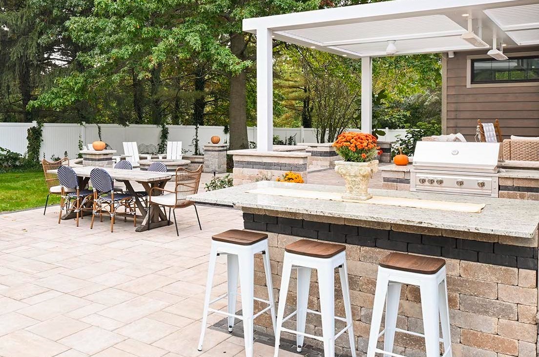 Outdoor kitchen and dining patio with built-in grill, bar seating, and modern pergola in a landscaped backyard in Ohio
