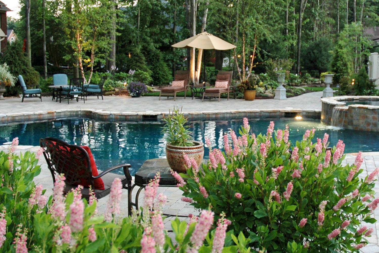 Inground pool with flowering garden plantings and a patio umbrella