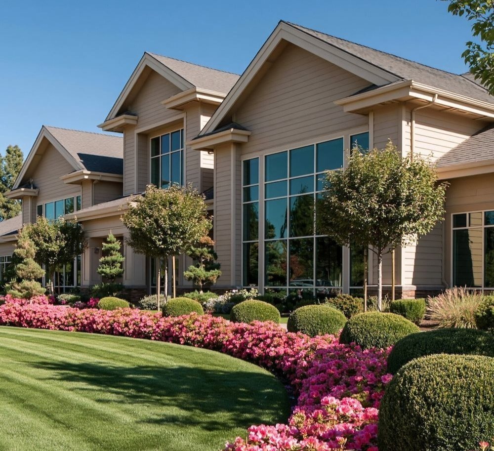 Professionally landscaped commercial property with manicured green lawn, vibrant pink flowering shrubs, ornamental trees, and neatly trimmed hedges