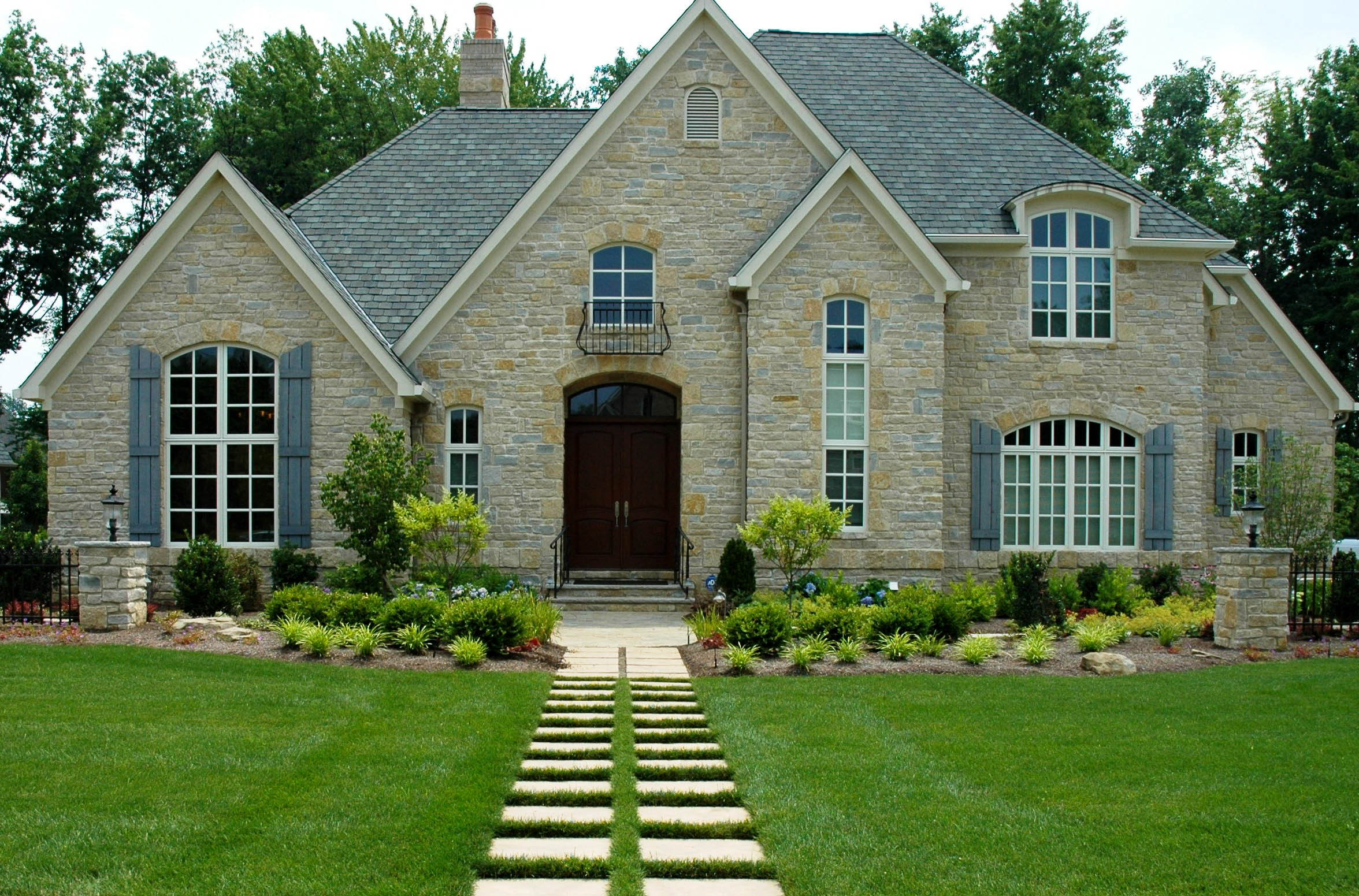 Stone home with a manicured lawn and landscaped garden beds