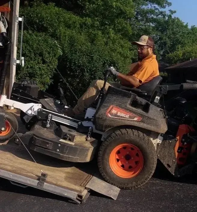Crew member unloading a zero-turn mower from a trailer