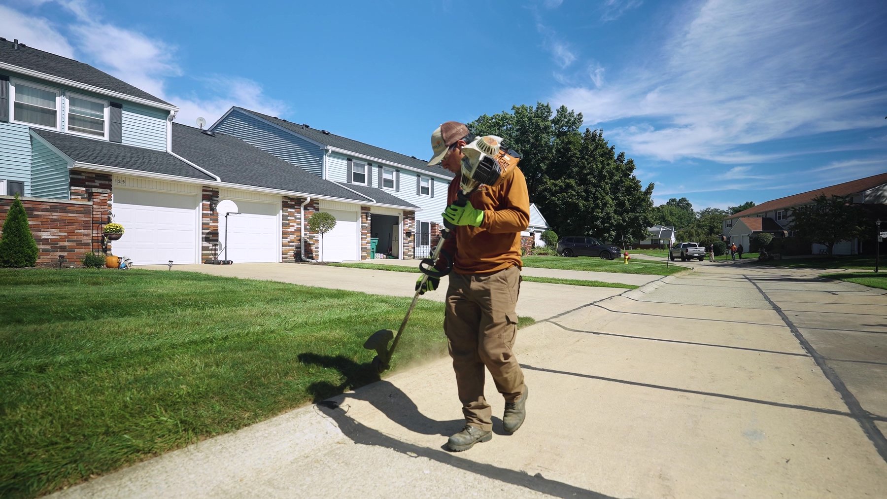 An exscape Group crew member trimming the grass in a residential front yard.